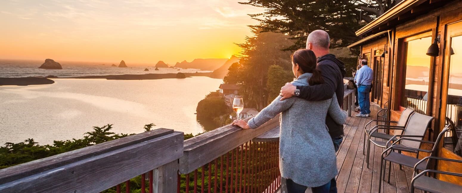 Couple in embrace watching a beautiful sunset alongside a glass of wine